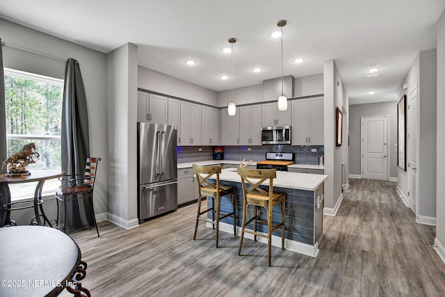 kitchen with gray cabinetry, stainless steel appliances, light countertops, light wood-style floors, and backsplash