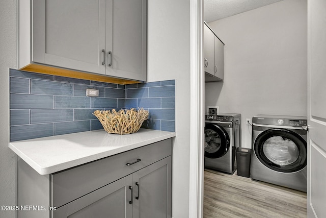 laundry area with cabinet space, a textured ceiling, light wood-style flooring, and washing machine and clothes dryer