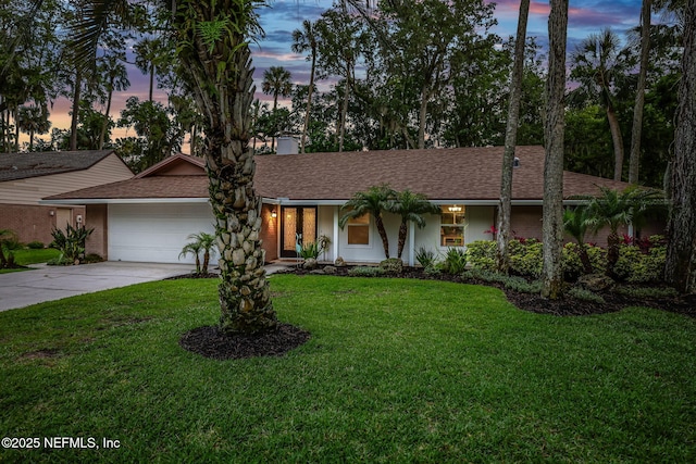 view of front facade with an attached garage, concrete driveway, a lawn, and a shingled roof