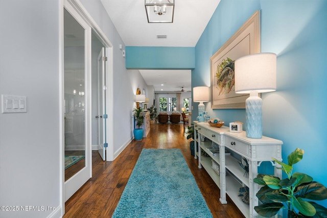 hall with dark wood-style flooring, visible vents, and baseboards