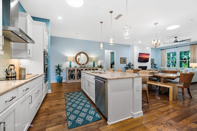 kitchen with stainless steel dishwasher, open floor plan, a sink, wall chimney range hood, and black electric cooktop