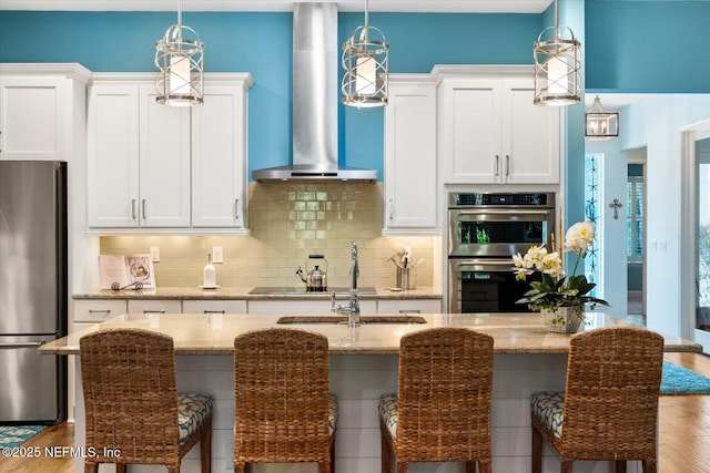 kitchen with a center island with sink, decorative backsplash, stainless steel appliances, wall chimney range hood, and a kitchen bar