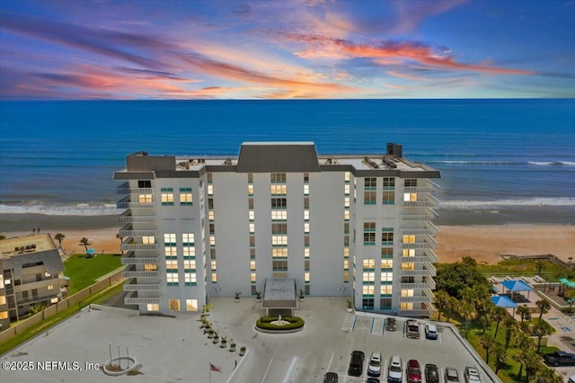 aerial view at dusk with a water view and a view of the beach