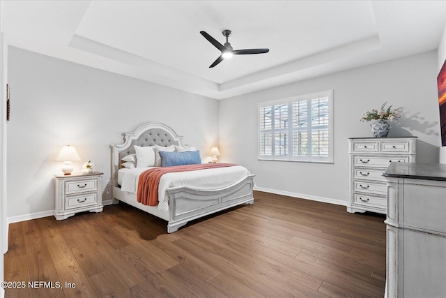 bedroom with ceiling fan, dark wood-style flooring, a raised ceiling, and baseboards