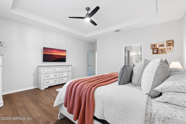 bedroom with a raised ceiling, visible vents, baseboards, and wood finished floors