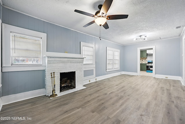 unfurnished living room featuring wood finished floors, a fireplace, visible vents, and ornamental molding