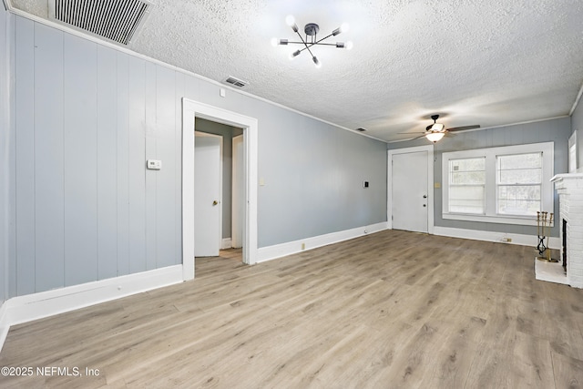 unfurnished living room featuring wood finished floors, visible vents, ceiling fan, a textured ceiling, and a brick fireplace