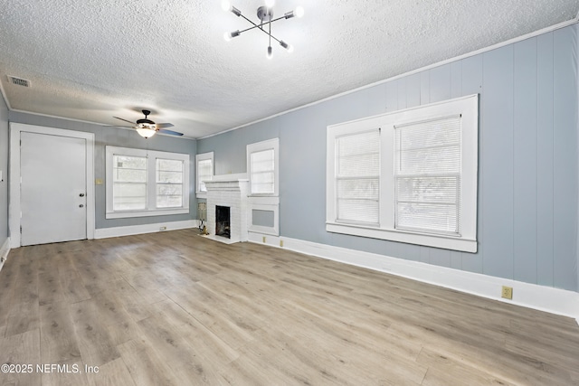 unfurnished living room featuring a ceiling fan, wood finished floors, visible vents, ornamental molding, and a brick fireplace