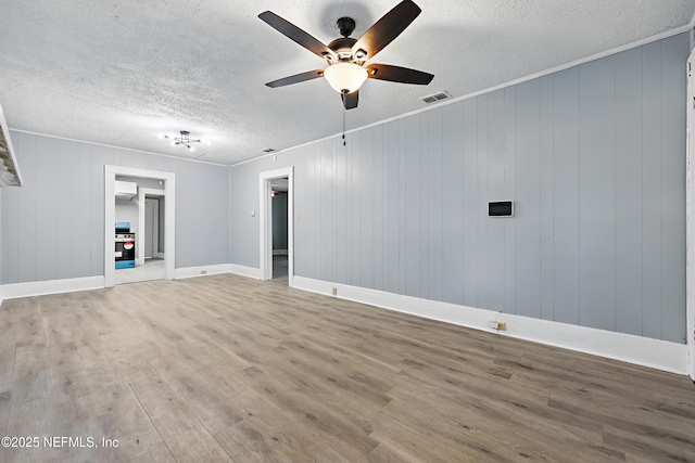 spare room with visible vents, a textured ceiling, wood finished floors, crown molding, and baseboards