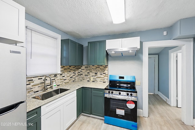 kitchen featuring freestanding refrigerator, a sink, electric stove, under cabinet range hood, and light wood-type flooring