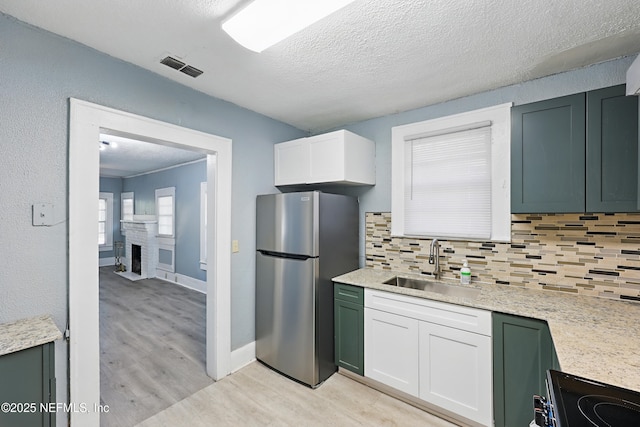 kitchen with visible vents, light wood-style flooring, a sink, freestanding refrigerator, and decorative backsplash