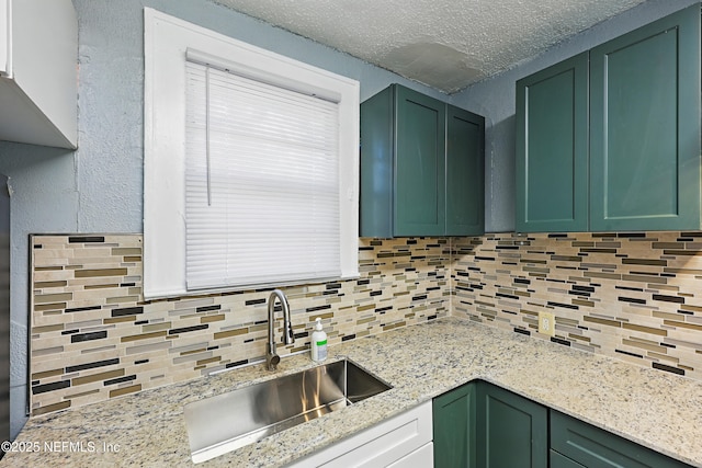 kitchen featuring green cabinets, a textured wall, tasteful backsplash, and a sink