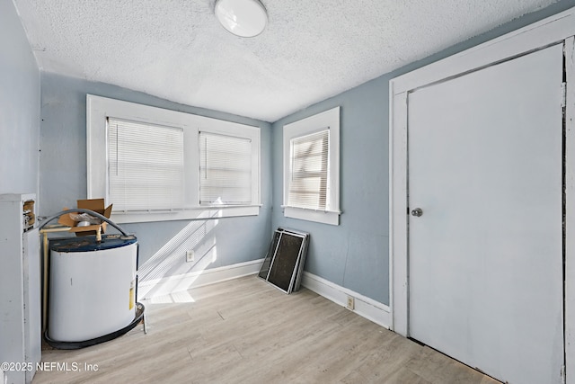 interior space with wood finished floors, baseboards, water heater, a closet, and a textured ceiling