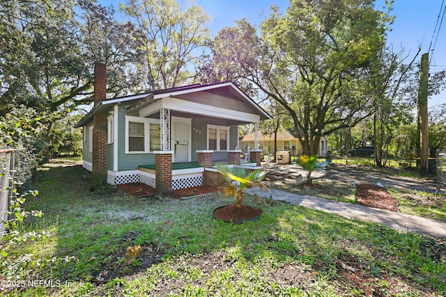 view of front of home featuring covered porch, a chimney, and fence