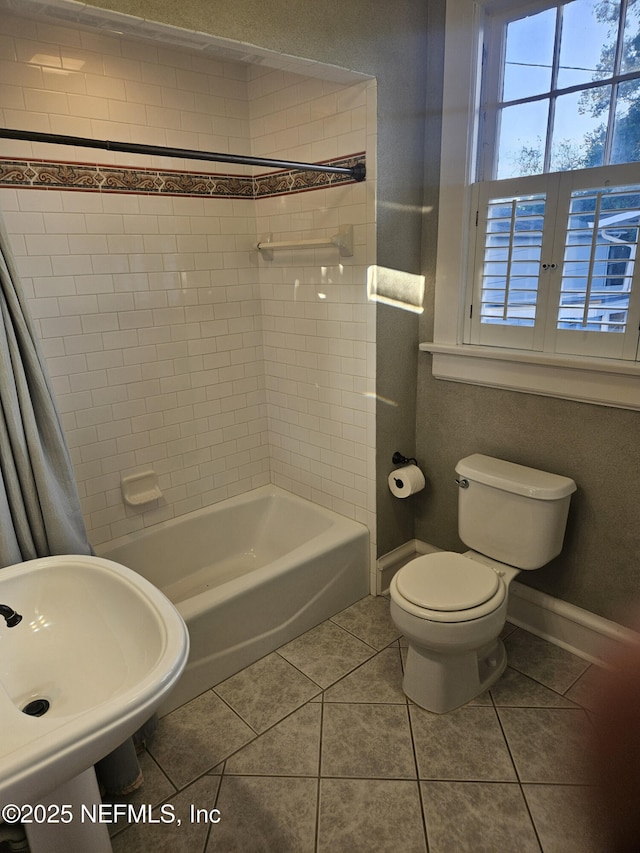 full bath featuring baseboards, toilet, shower / bathtub combination, tile patterned floors, and a sink