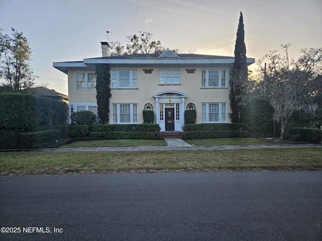 view of front of home featuring a yard, a chimney, and stucco siding