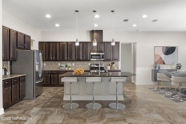 kitchen featuring dark brown cabinetry, visible vents, a kitchen breakfast bar, and stainless steel appliances