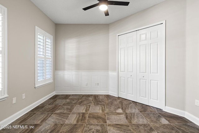 unfurnished bedroom featuring a wainscoted wall, a closet, and ceiling fan