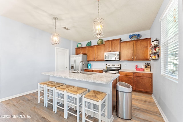 kitchen featuring visible vents, light wood-style flooring, brown cabinets, stainless steel appliances, and a sink