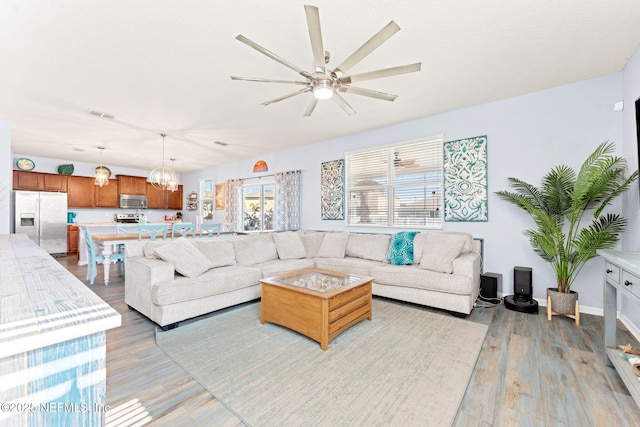 living area featuring light wood-type flooring, baseboards, visible vents, and ceiling fan with notable chandelier