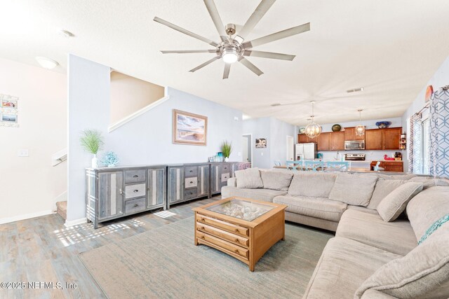 living room featuring stairs, visible vents, light wood-style floors, baseboards, and ceiling fan with notable chandelier