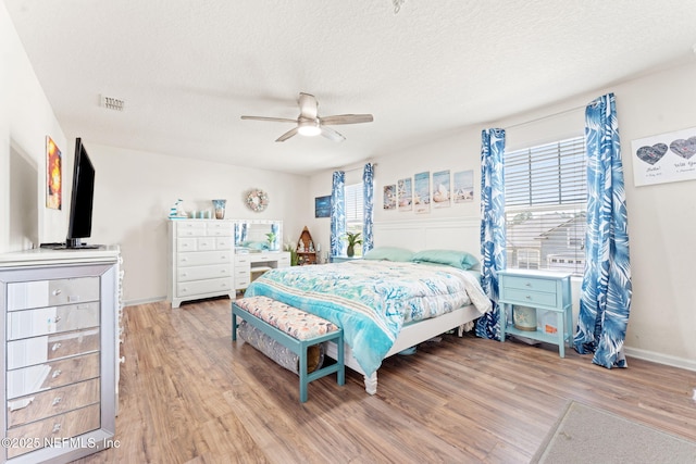 bedroom with a textured ceiling, multiple windows, wood finished floors, and visible vents