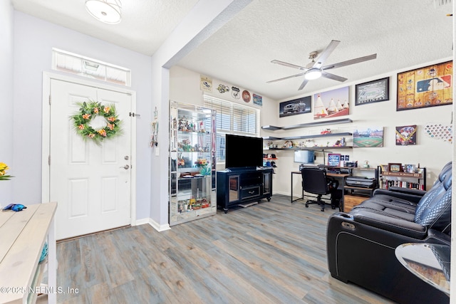 living area with a textured ceiling, wood finished floors, a ceiling fan, and baseboards