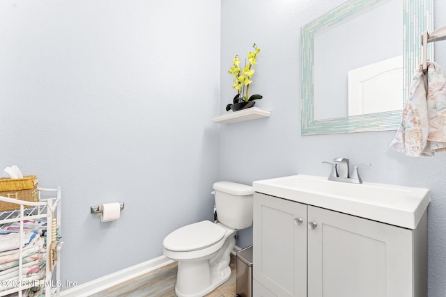 half bathroom with baseboards, vanity, toilet, and wood finished floors