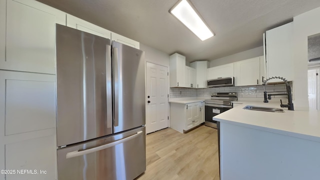 kitchen with light wood-style flooring, stainless steel appliances, a sink, light countertops, and backsplash