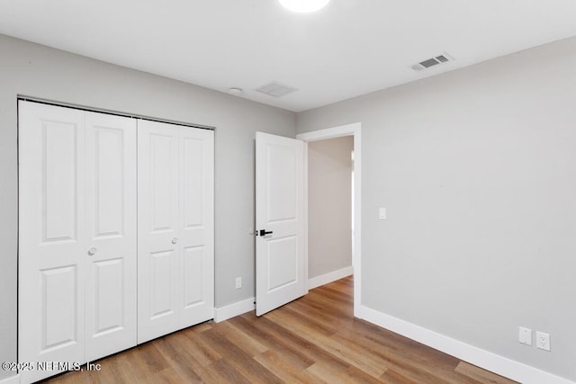 unfurnished bedroom featuring a closet, wood finished floors, visible vents, and baseboards