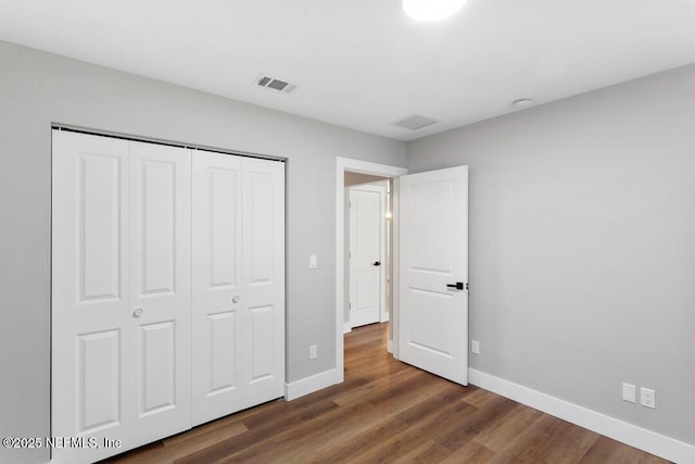 unfurnished bedroom with dark wood-type flooring, a closet, visible vents, and baseboards