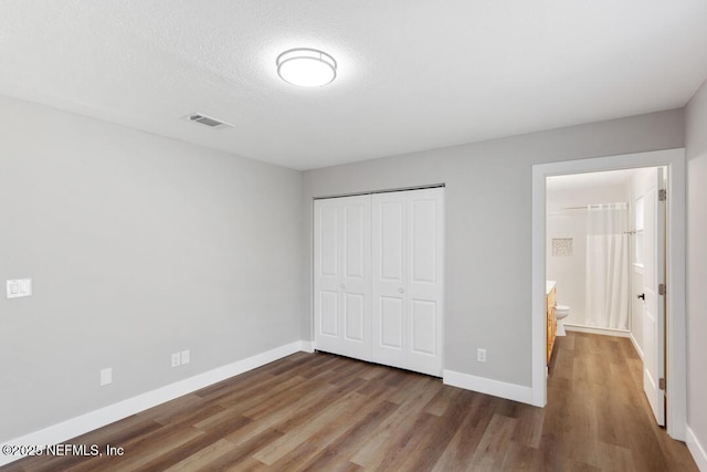 unfurnished bedroom featuring a closet, wood finished floors, visible vents, and baseboards