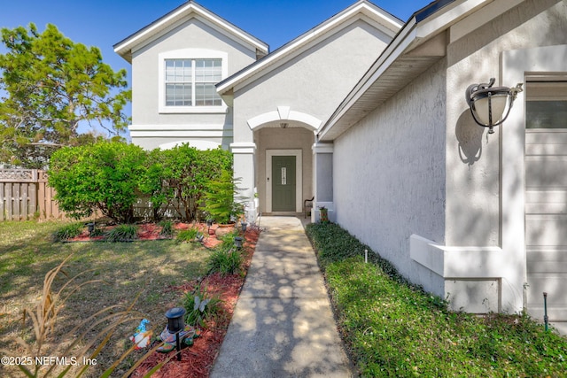 view of exterior entry with fence and stucco siding