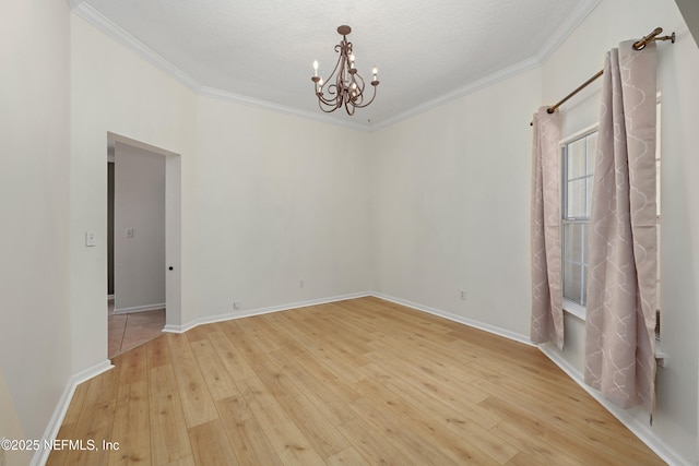 spare room featuring a notable chandelier, wood-type flooring, baseboards, and crown molding