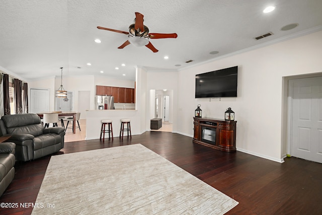 living room with dark wood-type flooring, vaulted ceiling, visible vents, and crown molding