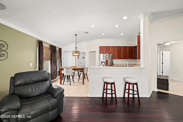 kitchen featuring stainless steel fridge with ice dispenser, ornamental molding, a breakfast bar area, open floor plan, and vaulted ceiling