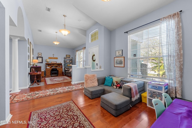 living room with wood finished floors, visible vents, decorative columns, a fireplace, and vaulted ceiling