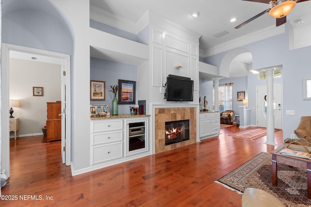 living area featuring hardwood / wood-style floors, a fireplace, crown molding, ceiling fan, and ornate columns