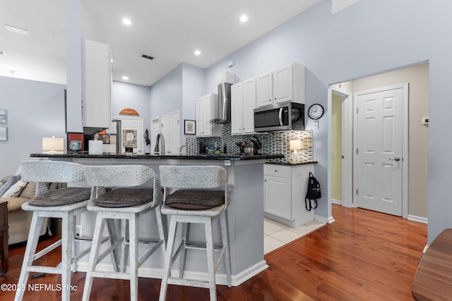 kitchen with a breakfast bar, light wood-style flooring, stainless steel microwave, wall chimney exhaust hood, and backsplash