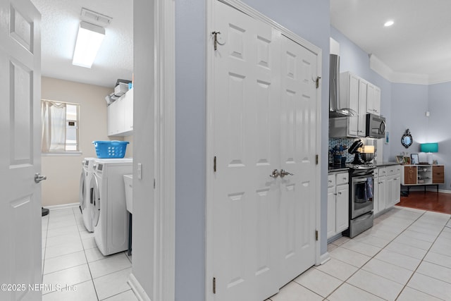 interior space with stainless steel electric stove, light tile patterned floors, washer and dryer, white cabinetry, and wall chimney exhaust hood