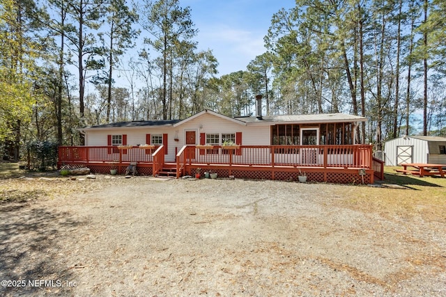 rear view of property with driveway, a wooden deck, an outdoor structure, and a storage unit