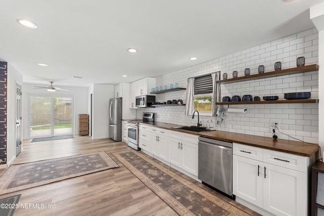 kitchen with light wood finished floors, wood counters, appliances with stainless steel finishes, open shelves, and a sink