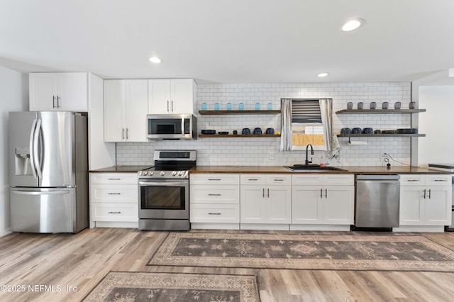 kitchen with open shelves, appliances with stainless steel finishes, light wood-type flooring, and a sink