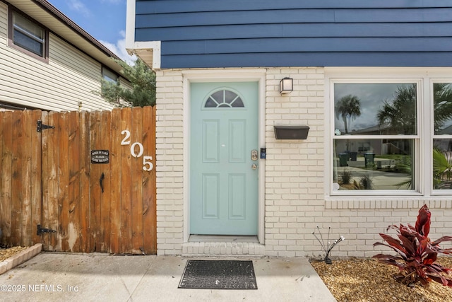 view of exterior entry with brick siding and fence