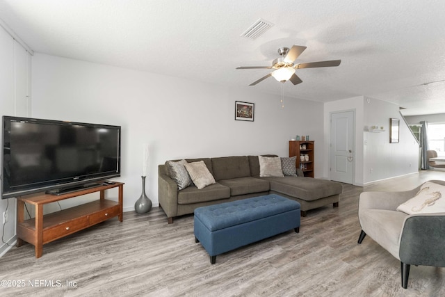 living area with a textured ceiling, ceiling fan, light wood finished floors, and visible vents