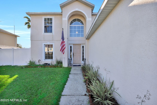 entrance to property featuring stucco siding, a lawn, and fence