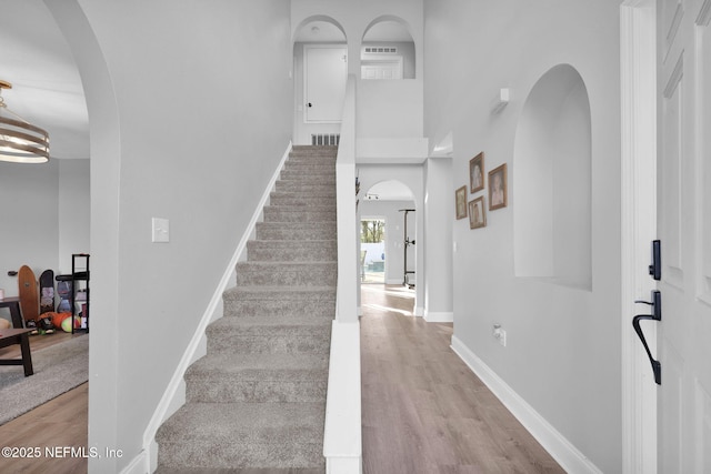 stairs featuring visible vents, baseboards, a high ceiling, wood finished floors, and arched walkways