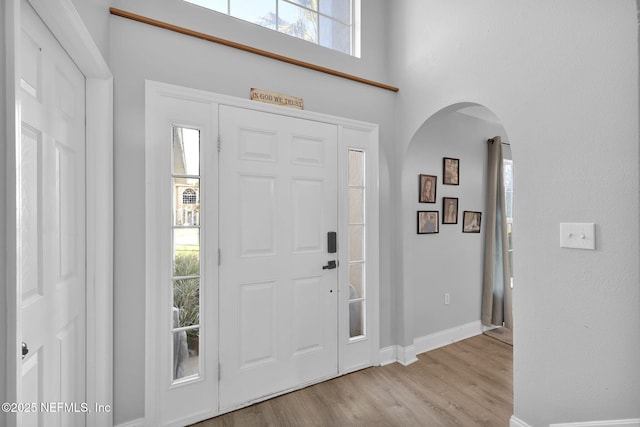 entrance foyer with light wood-type flooring, arched walkways, baseboards, and a towering ceiling