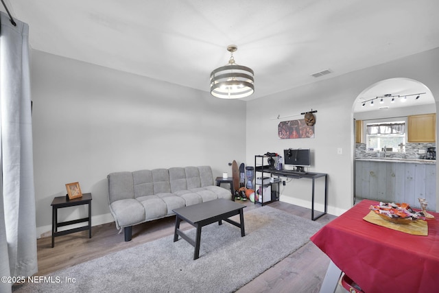 living area with visible vents, wood finished floors, arched walkways, baseboards, and a chandelier