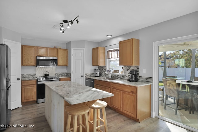 kitchen with light wood-style flooring, a sink, a kitchen island, stainless steel appliances, and decorative backsplash